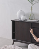 Dark wooden sideboard with decorative vases and a plant against a light gray wall.