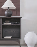Dark wooden side table with a lamp and decorative items against a white wall.