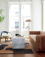 Modern living room with a brown sofa, marble coffee table, and large windows.