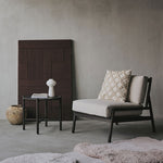 Modern lounge chair with a textured pillow against a gray wall.