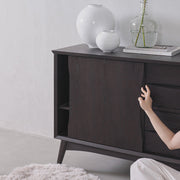 Dark wooden sideboard with decorative vases and a plant against a light gray wall.