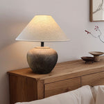 Table lamp with a textured base on a wooden side table against a neutral wall.
