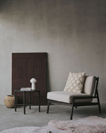 Modern lounge chair with a textured pillow against a gray wall.