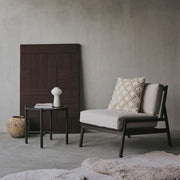 Modern lounge chair with a textured pillow against a gray wall.